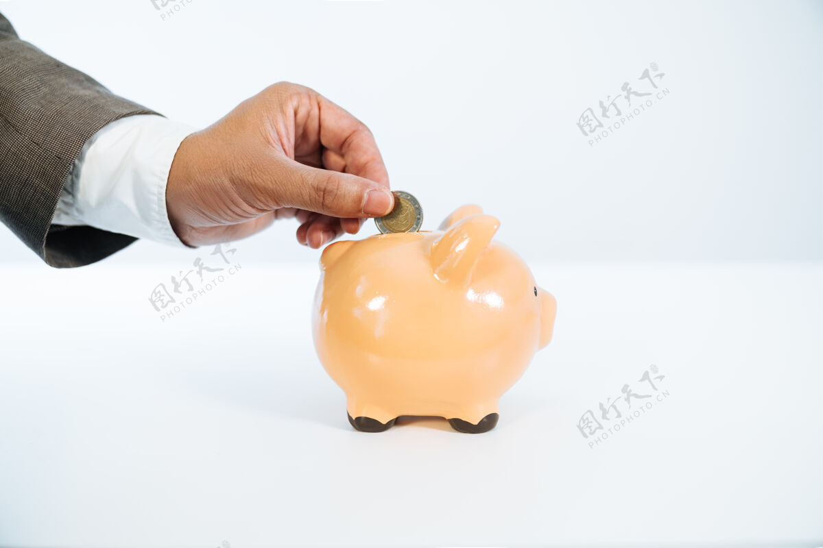 持有一只手把一枚硬币放进一个白色背景和非常好的光线的陶瓷存钱罐的侧视图贷款投资问题