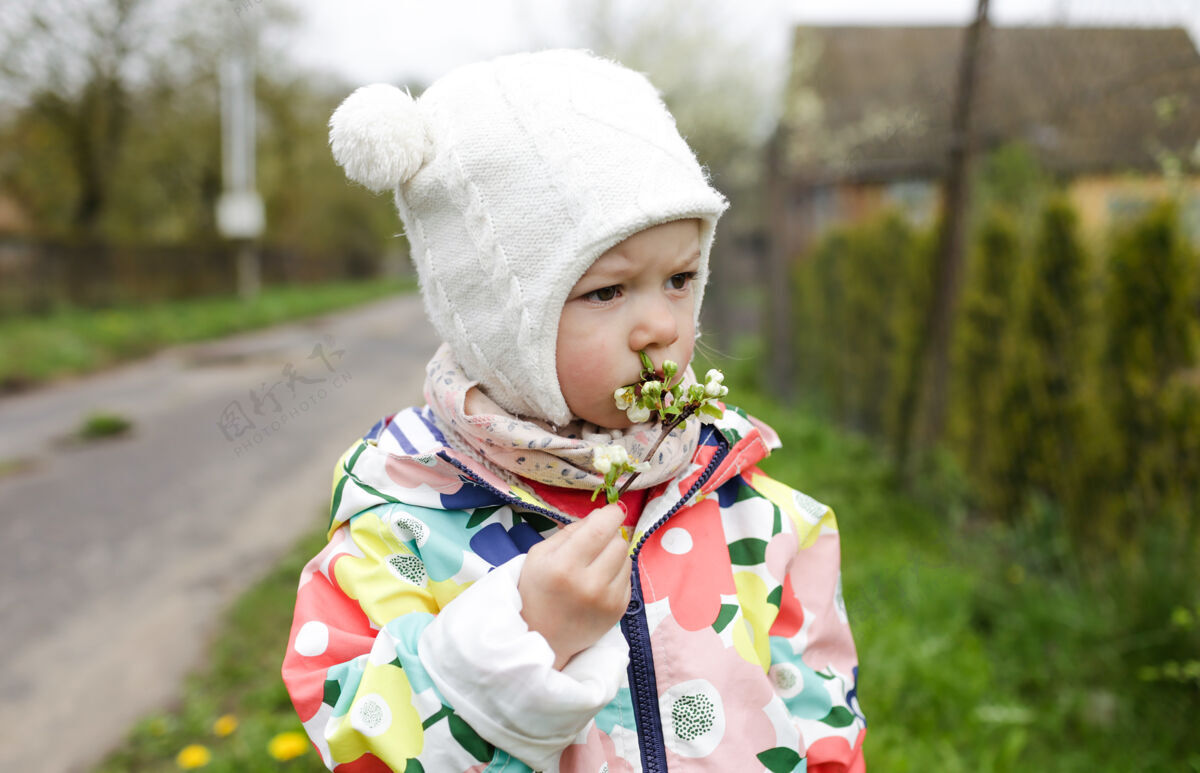 站春天里 一个穿着鲜艳夹克的小女孩站在外面 手里拿着一枝春天开的白花春天玩夹克