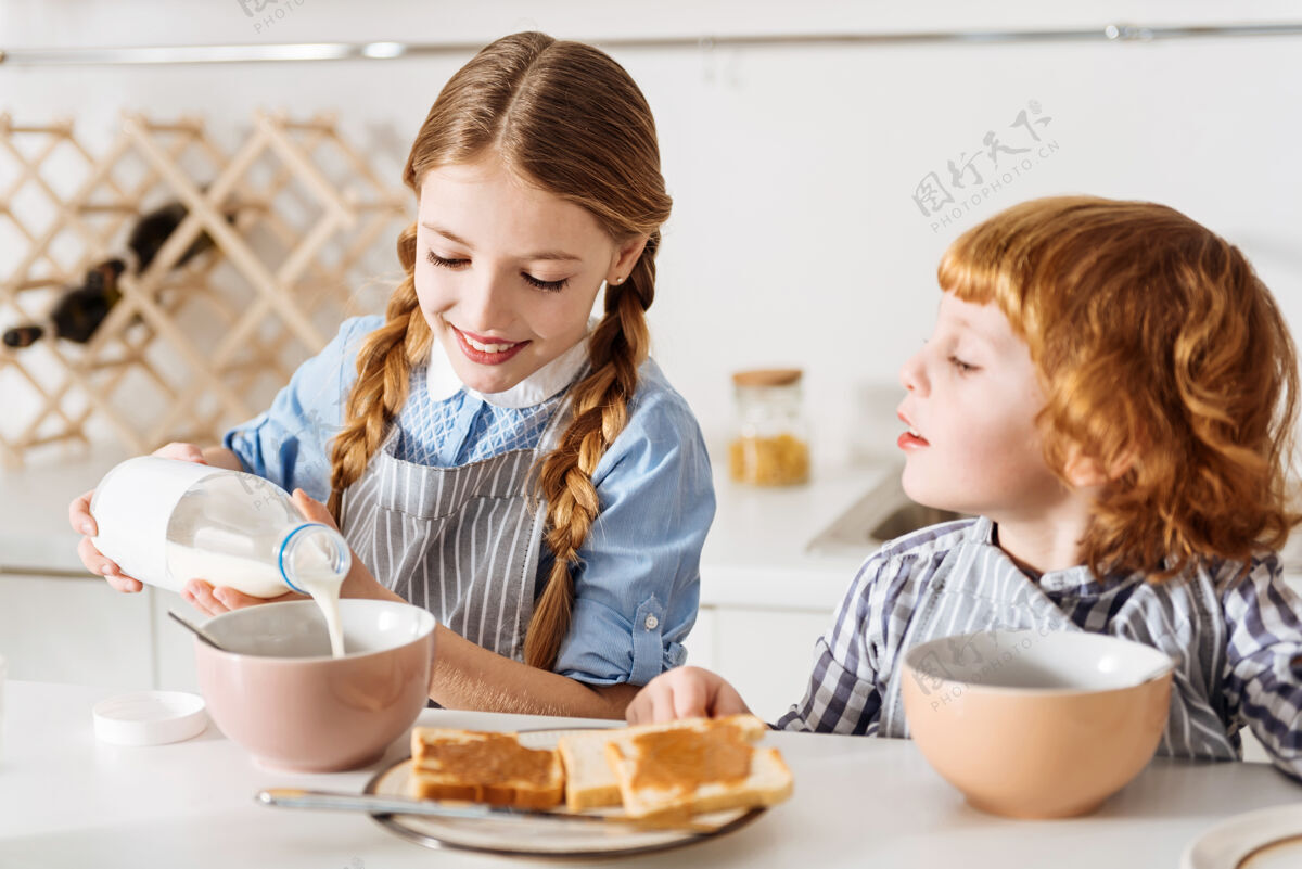 准备容易的烹饪漂亮令人钦佩的可爱的孩子和她的哥哥一起吃早餐 在她的碗里煮牛奶 而他们都坐在厨房的桌子旁麦片兴奋国内