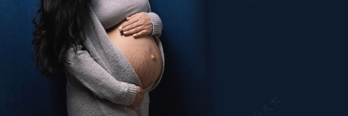 等待年轻孕妇在蓝色背景上触摸腹部 婴儿等待概念期望肚子产妇