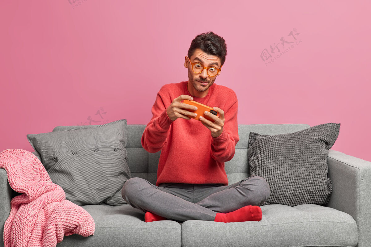 粉色上瘾的男人在智能手机上玩网络游戏 盘腿坐在舒适的沙发上地板坐着公寓