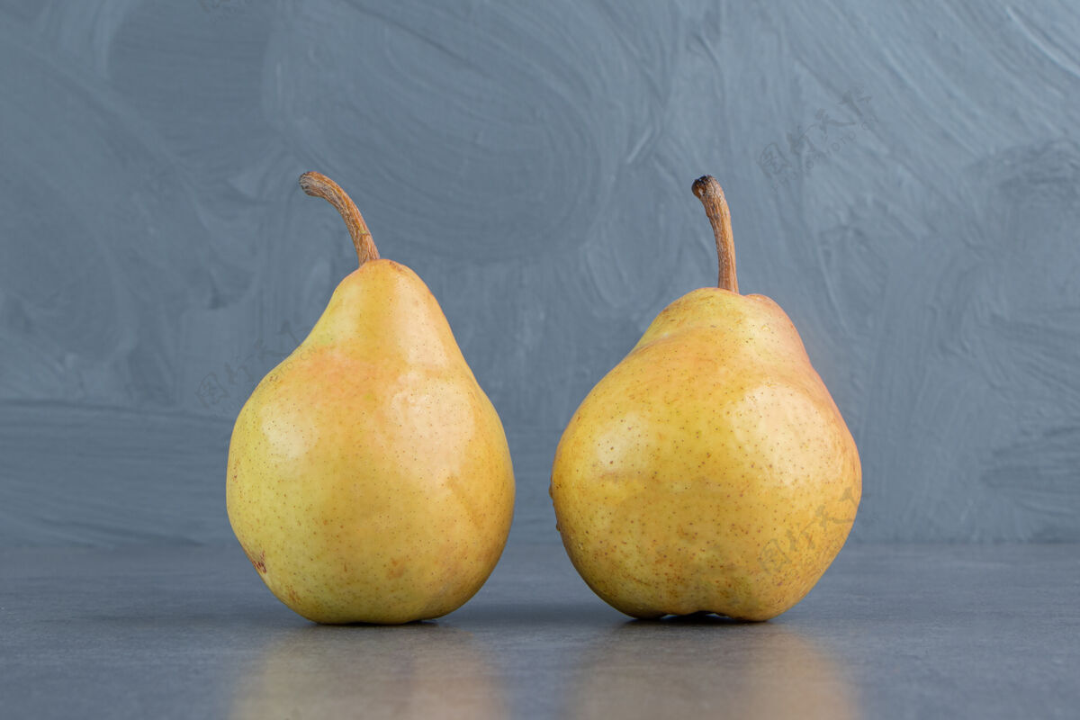 饱满两个成熟的红黄色的梨果实被隔离在一个灰色的表面上食物生的美味
