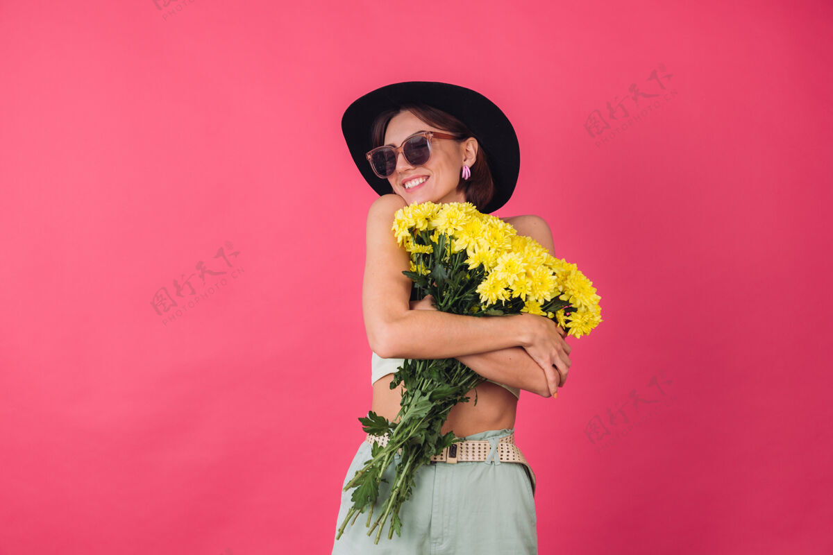肖像戴着帽子和墨镜的时髦女人 拥抱着一大束黄紫苑 春意盎然 淡定微笑的孤立空间自然长深色