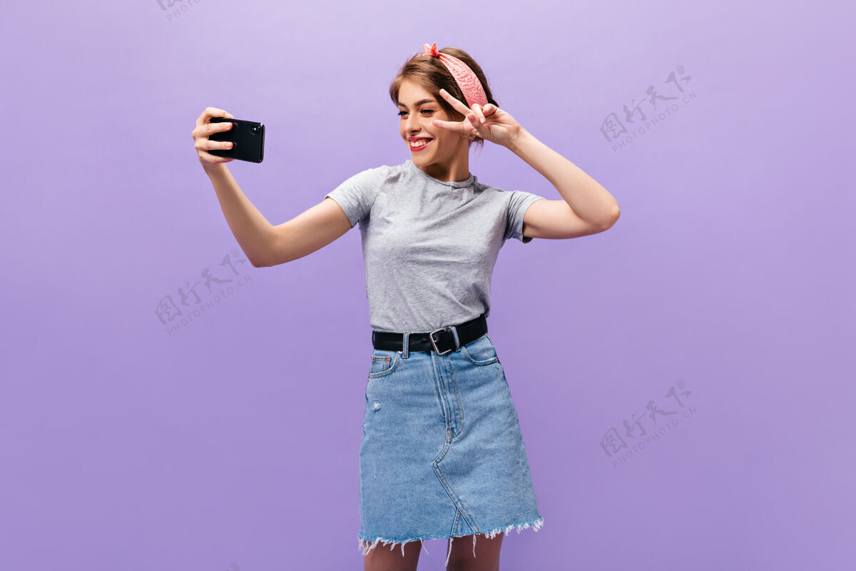 复制展示和平标志的女孩 在紫色背景上眨眼和自拍穿着时髦服装摆姿势的漂亮年轻女子头发姿势紫色