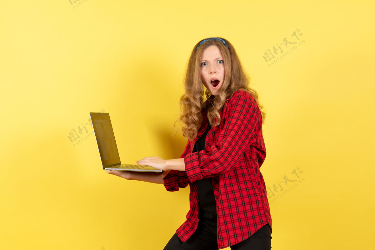 人正面图身着红色格子衬衫的年轻女性用笔记本电脑在黄色背景上演绎女性人情模特的时尚女孩微笑情绪漂亮