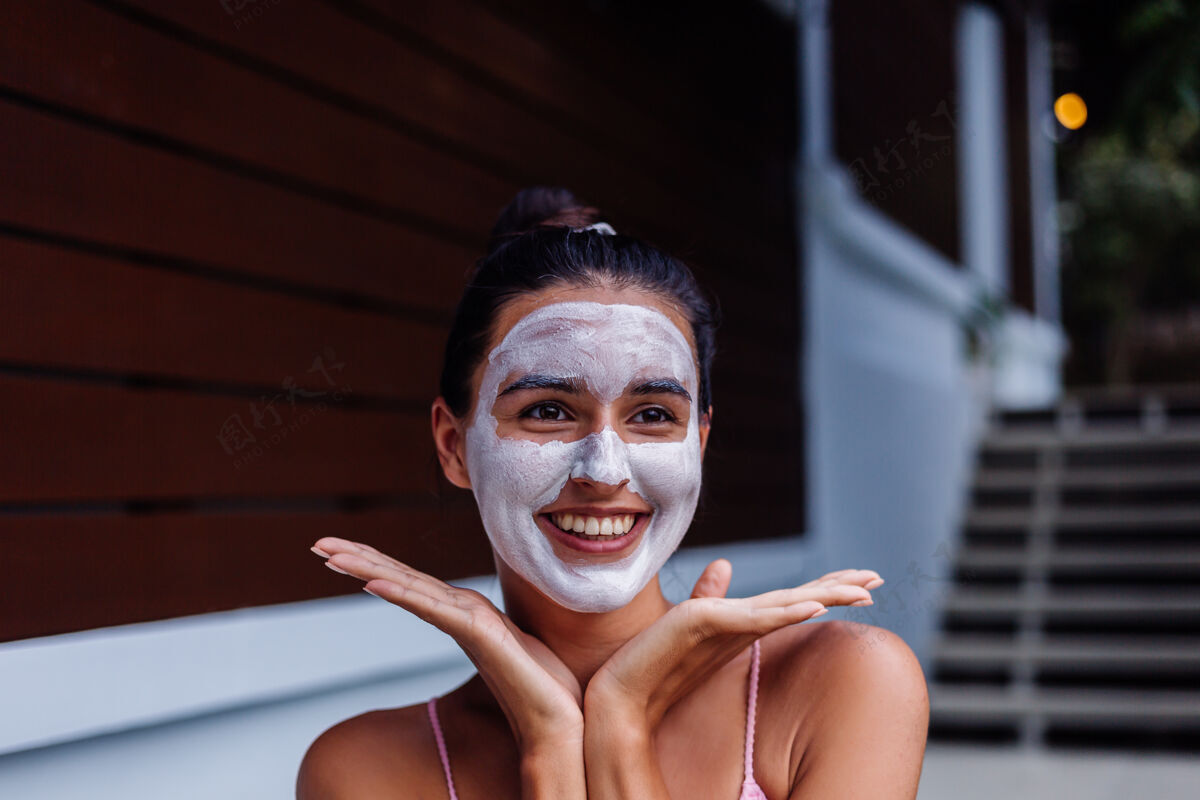 旅行晒黑皮肤的户外写真美丽的高加索女子穿着比基尼在温泉浴场与白色脱皮面具在脸上肖像水疗面部