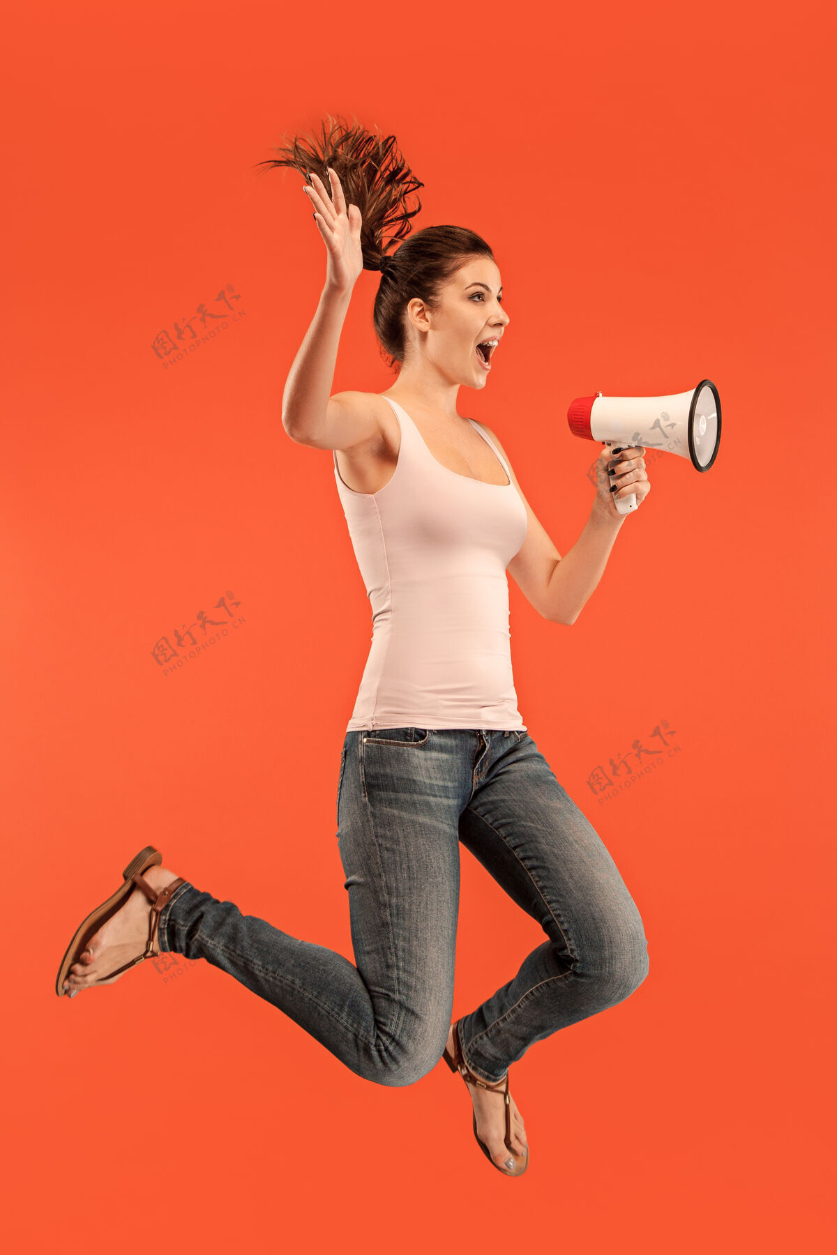 交流美丽的年轻女子用扩音器在红色背景上孤立地跳跃奔跑的女孩在运动或运动黑发扩音器兴奋