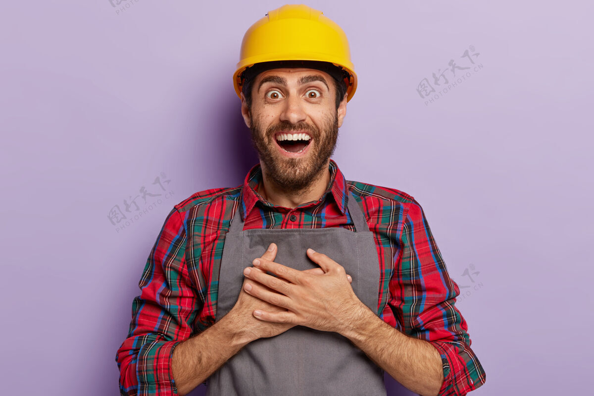 工人积极向上的快乐建设者 在建筑公司工作 双手放在胸前 戴黄色安全帽 工作服 笑容灿烂快乐制服安全帽