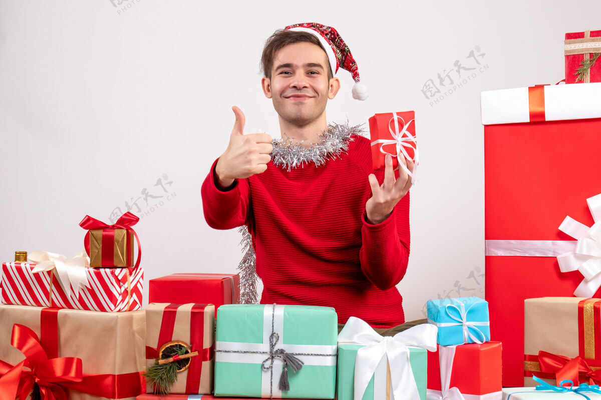 年轻人前视图年轻人做拇指向上的标志坐在周围的圣诞礼物购物男人拇指