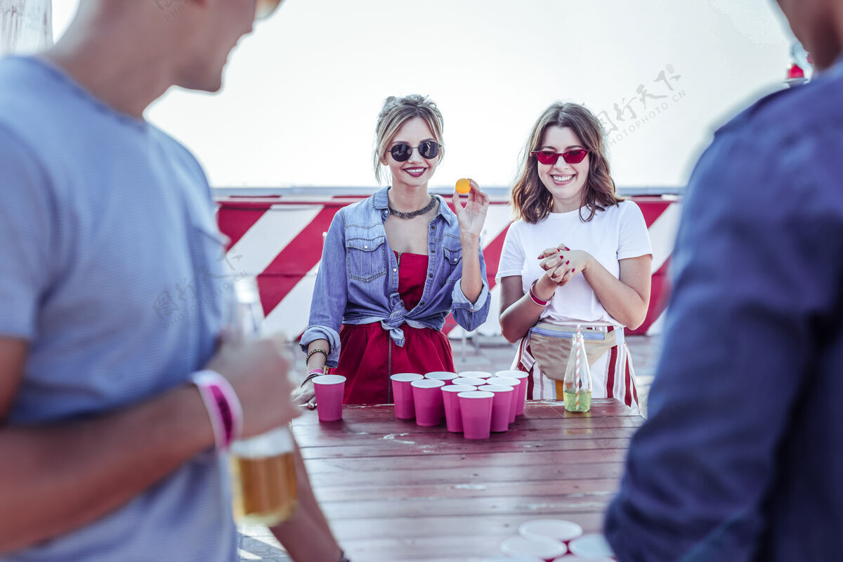屋顶桌上游戏快乐的女孩脸上保持微笑 同时看着他们的合作伙伴啤酒互动社交