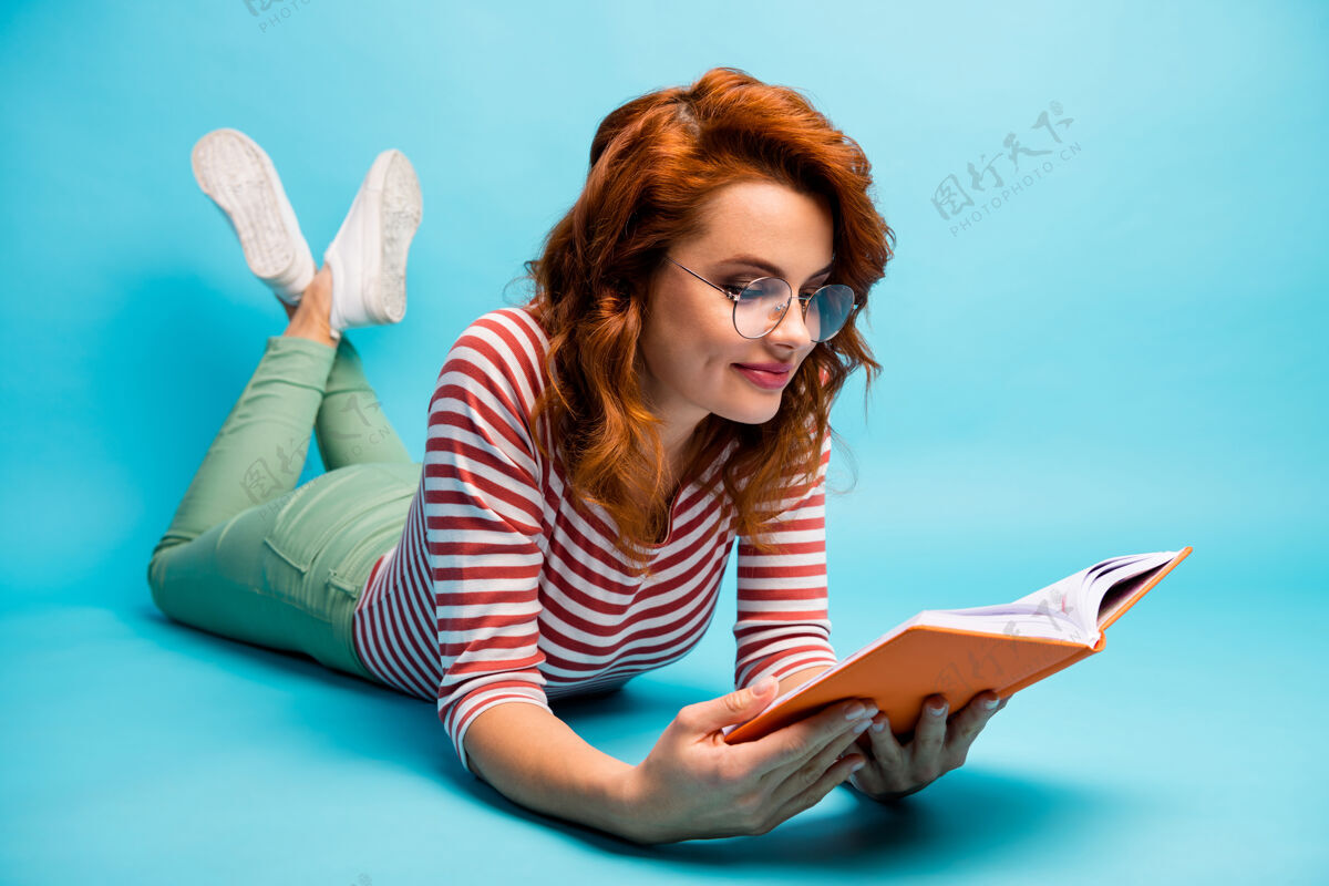 学习全身特写照片积极女孩躺在地板上读诗享受休息放松穿好看的套头衫隔离蓝色学校头发阅读