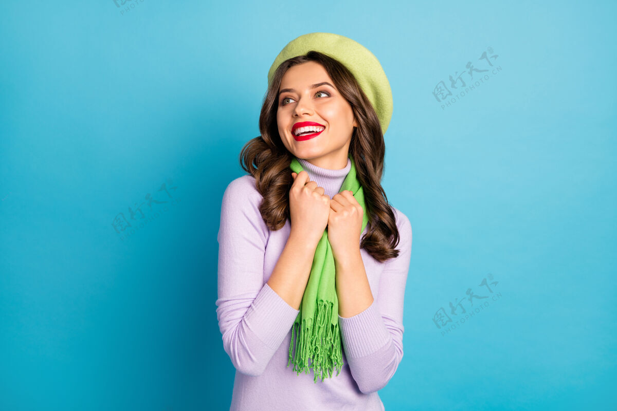 休闲美女的特写照片红唇牙齿微笑好心情调情看空空间戴绿色贝雷帽紫色高领围巾隔离蓝色墙壁欢乐女孩漂亮