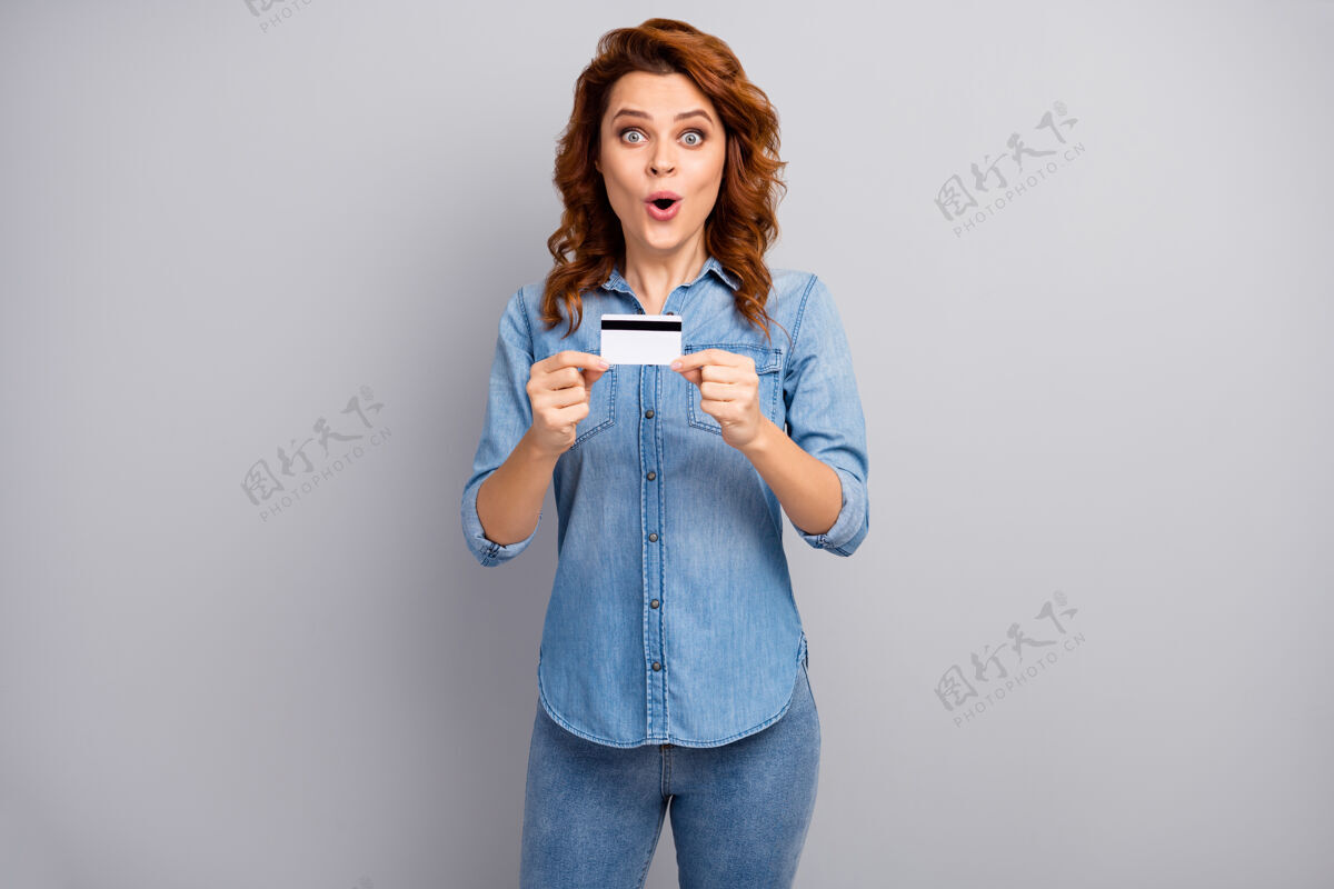 付款照片中惊讶的女人拿着信用卡 被银行网上支付系统打动 哇哦 天哪 穿上好看的衣服 隔着灰色的墙女人时尚时尚