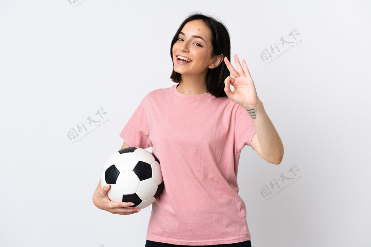 训练年轻的白种女人 拿着足球和ok标志 被隔离在白色背景下墙青年手势