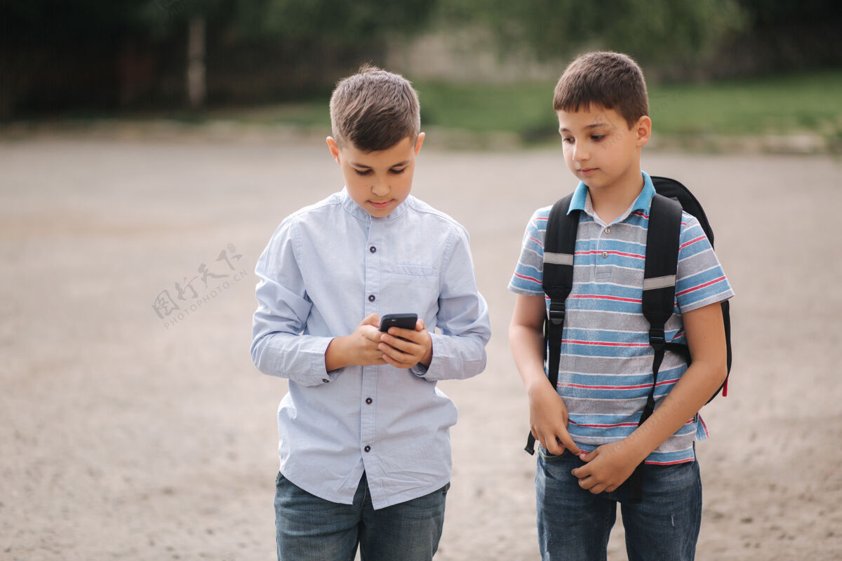 年轻人两个男孩在隔离区玩网络游戏小男孩微笑着打电话一个看怎么玩另一个手机休闲户外