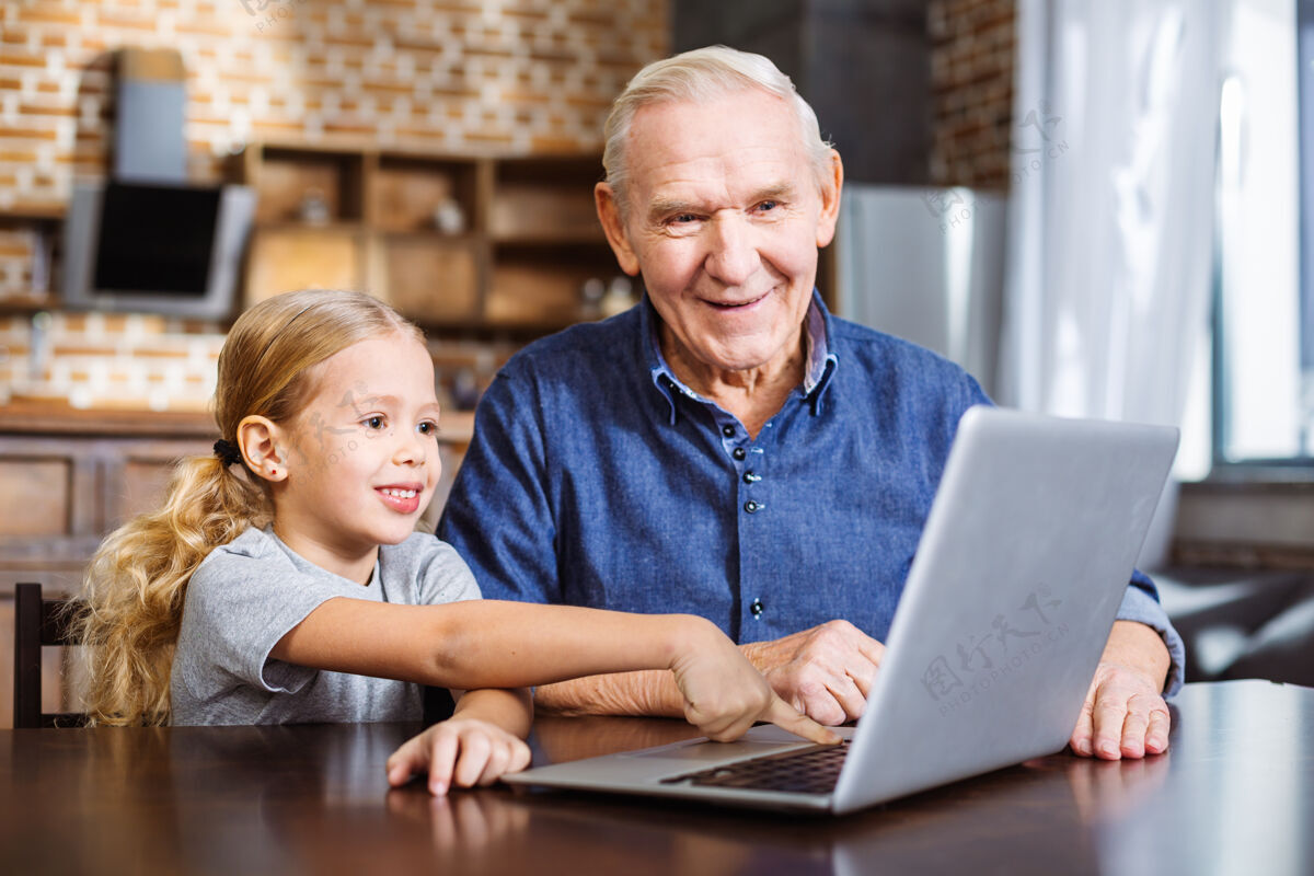 女儿快乐的小女孩指着屏幕 和爷爷一起用笔记本电脑在线休闲笔记本电脑