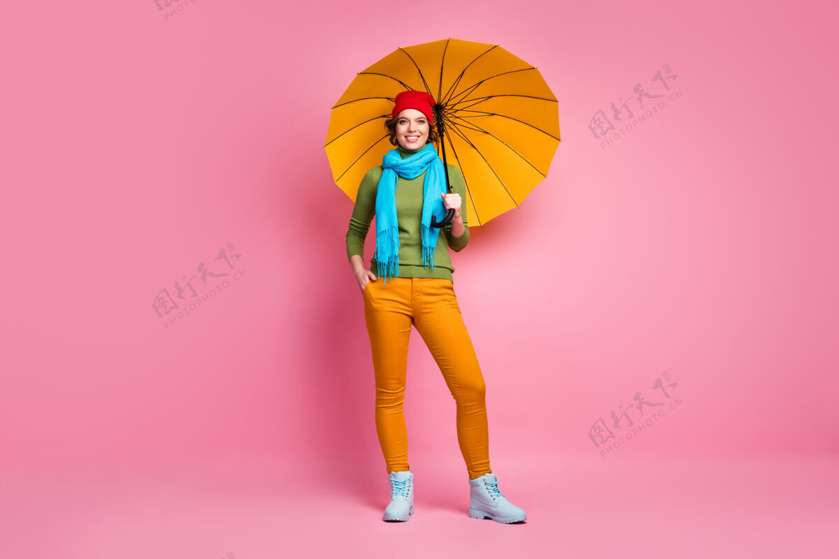 女性快乐女孩的全尺寸照片拿着她明亮的黄色阳伞享受季节自由时间旅行穿套头衫裤子鞋子隔着粉红色的墙颜色鞋子散步