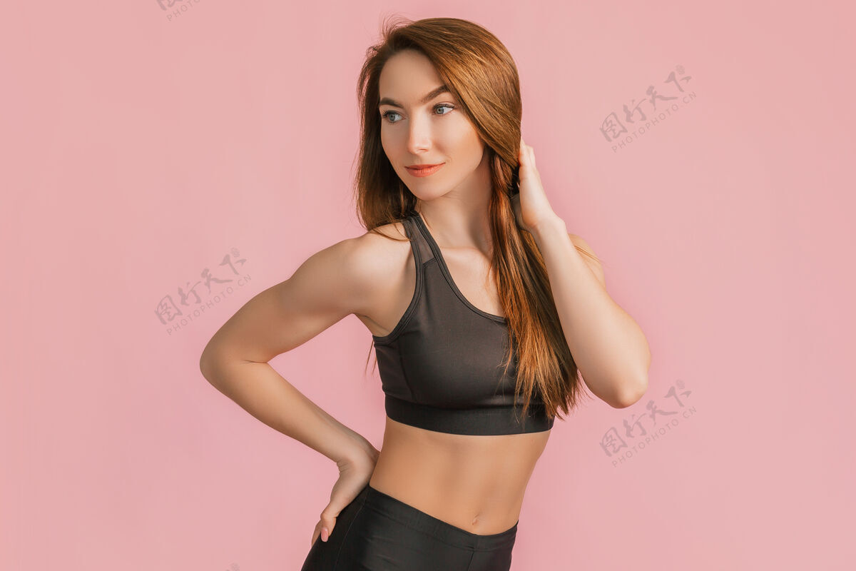 减肥在粉红色的空间里 一个穿着黑色运动服微笑的健身女孩体重动机拉