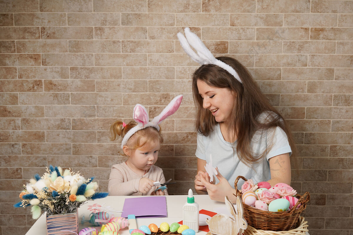 孩子美丽的年轻女子和可爱的小女孩正在准备复活节庆典妈妈和戴着兔子耳朵的女儿在家里玩得很开心童年兔子坐着