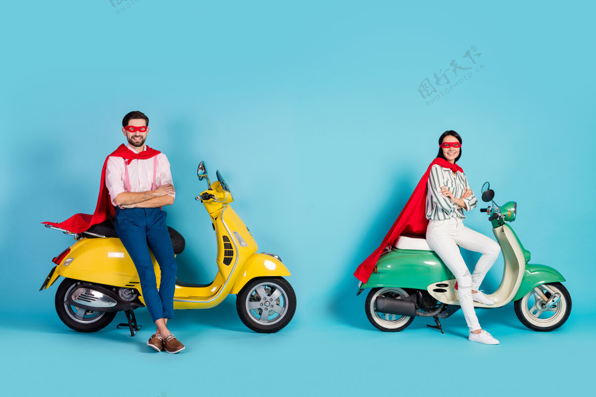 时尚全尺寸搞笑淑女男双臂交叉坐在两辆老式轻便摩托车上戴红色斗篷面具准备万圣节派对扮演超级英雄角色蓝色隔离墙女性男朋友男人