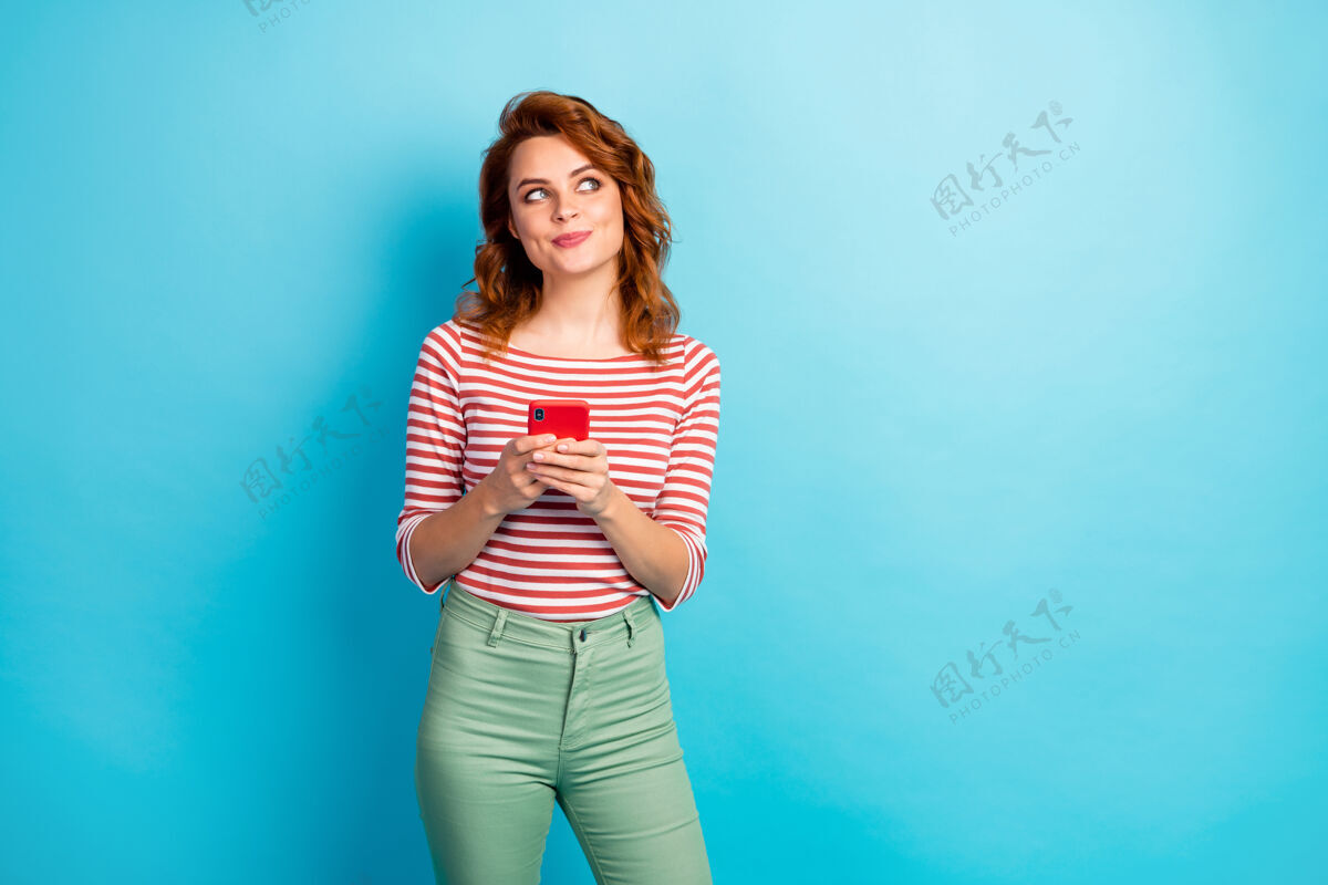 女孩好奇正面女孩的肖像使用智能手机看复制空间思考想法发布社交媒体新闻穿时尚毛衣隔离蓝色手机红发头发