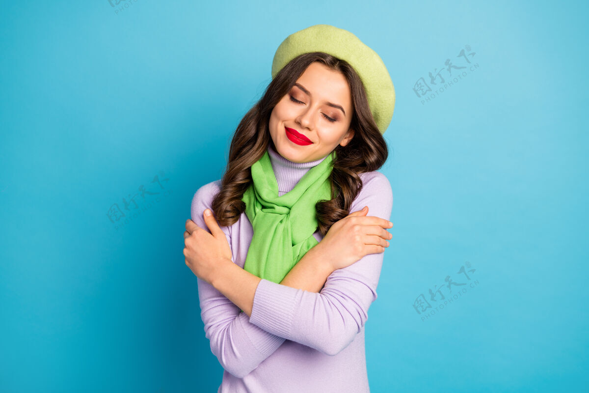 肩膀可爱女士的特写照片红唇闭上眼睛拥抱自己内心和谐的和平概念戴绿色贝雷帽紫色高领围巾蓝色隔离墙她自己可爱时尚