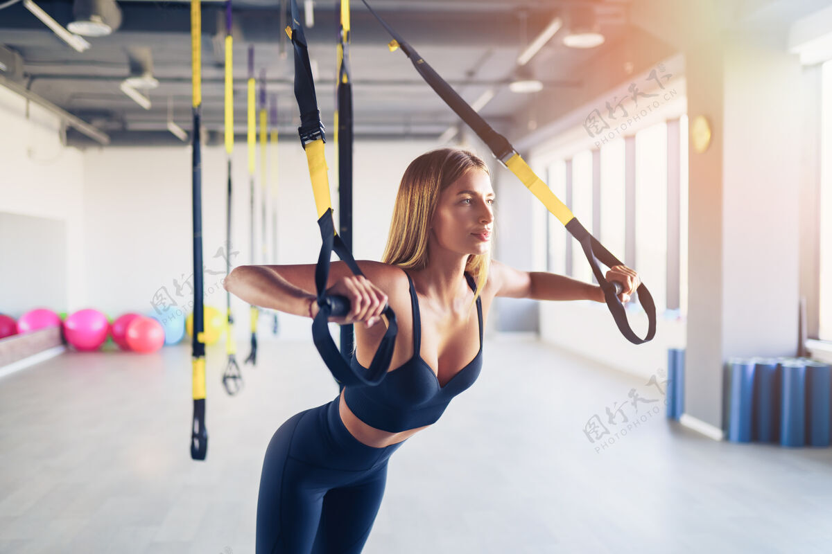 拉伸美丽的年轻女子训练与悬挂教练吊索或吊带在健身房上半身运动概念在trx上健康肌肉推
