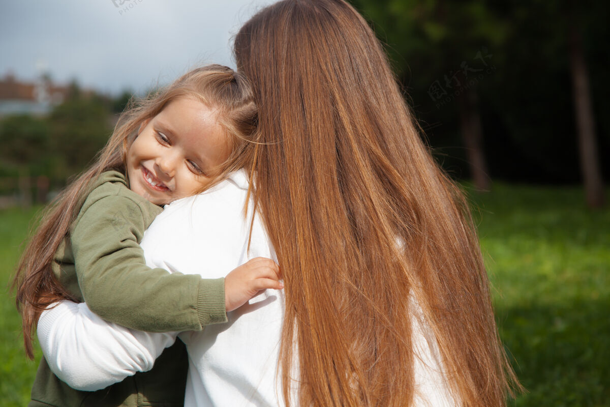 母亲在阳光明媚的日子里 一位年轻女子抱着她的女儿在公园里育儿理念孩子母亲照顾孩子妈妈