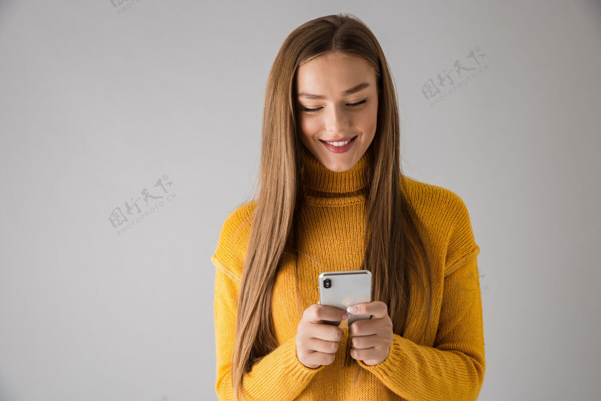 短信一个美丽快乐的年轻女子用手机隔着灰色的墙被孤立的画面手机站着爱