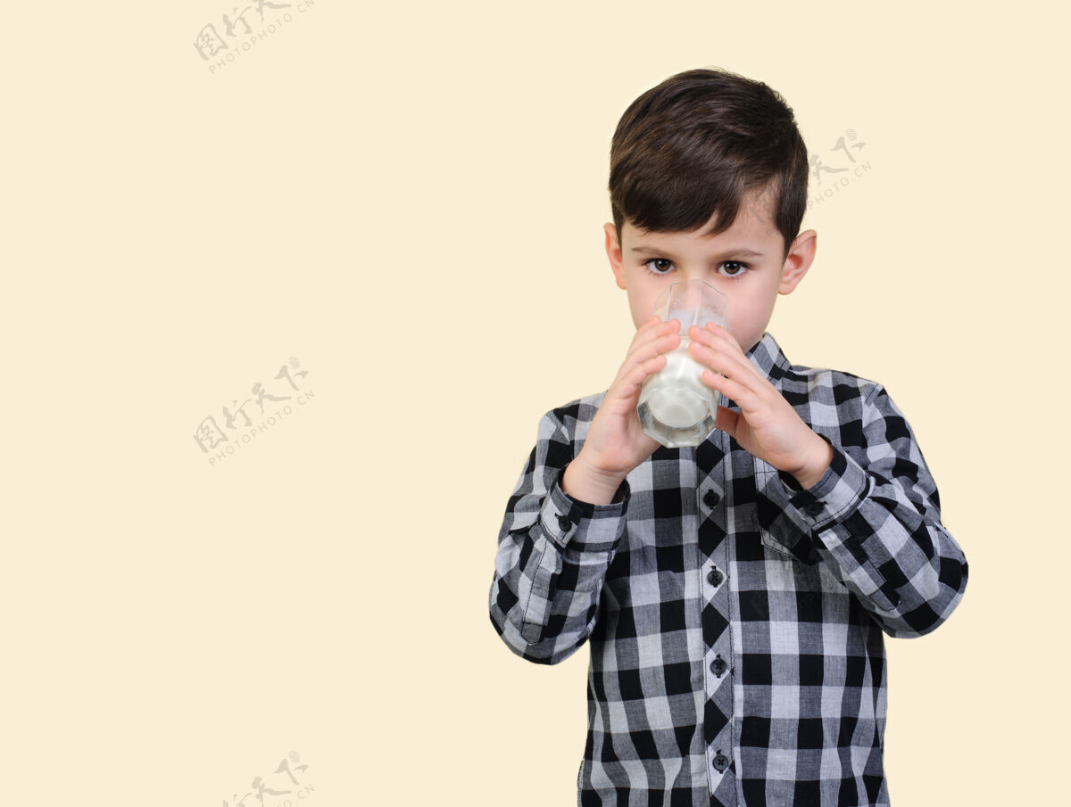 抱着6岁的男孩穿着灰色格子衬衫 在工作室米色背景上喝着杯子里的牛奶乳制品儿童肖像