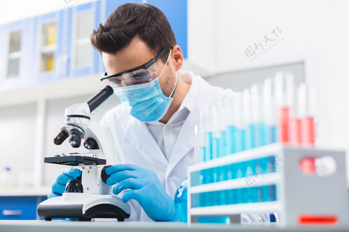 分析困难的任务认真熟练的男性实验室助理戴着口罩触摸显微镜和进行研究科学家情感实验室外套