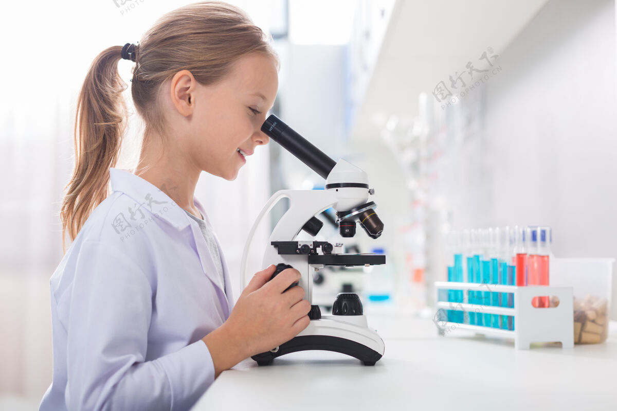 纯洁性伟大的乐器吸引人的野心勃勃的美丽女孩在侧面摆姿势 同时看着显微镜和触摸它学习智能科学