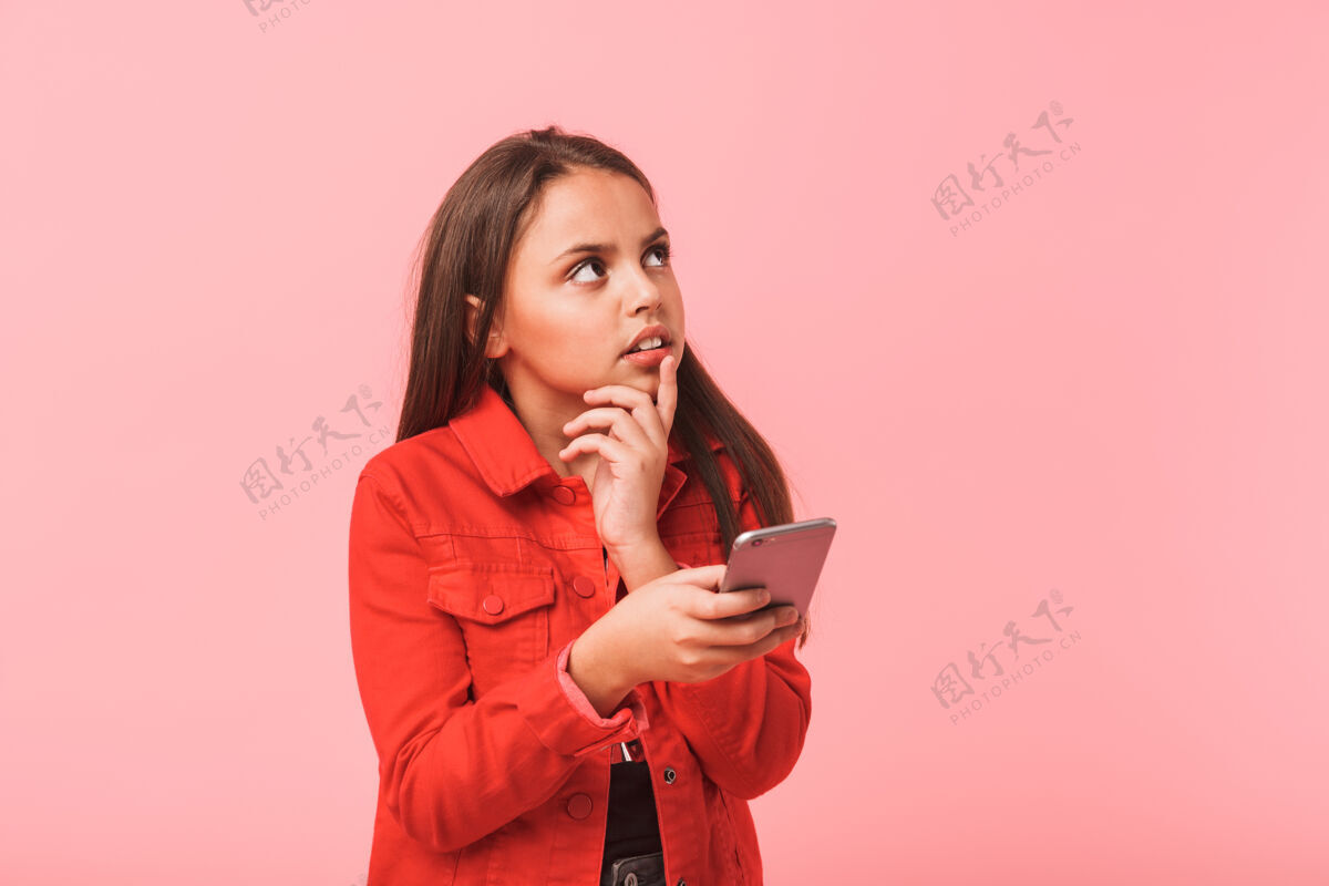 肖像迷惑不解的少女在随意使用手机的形象 而站在红墙隔离手机快乐黑发
