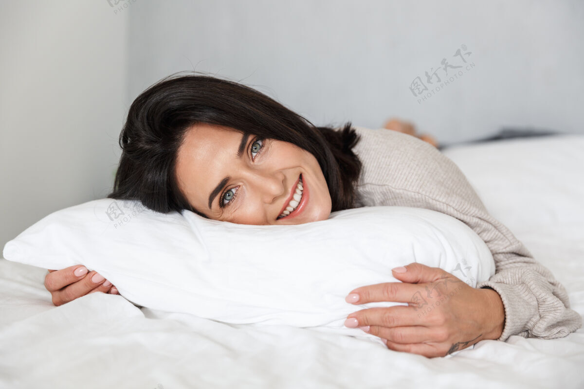 室内图为30多岁的快乐女人微笑着躺在床上 家里穿着白色亚麻布肖像沙发谎言