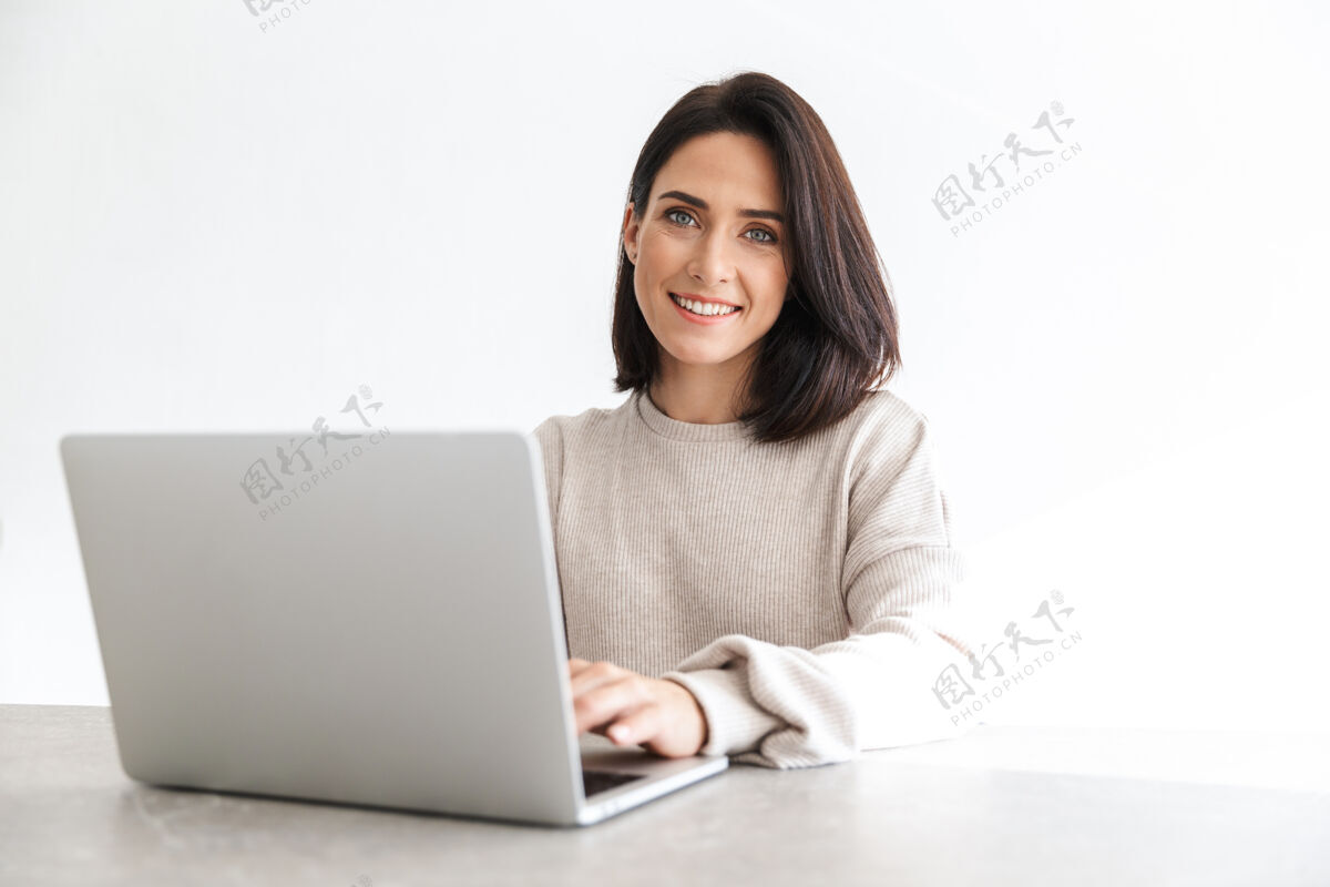 公寓可爱的女人30多岁的工作笔记本电脑 而坐在白色的墙壁在明亮的房间公寓成人笔记本电脑