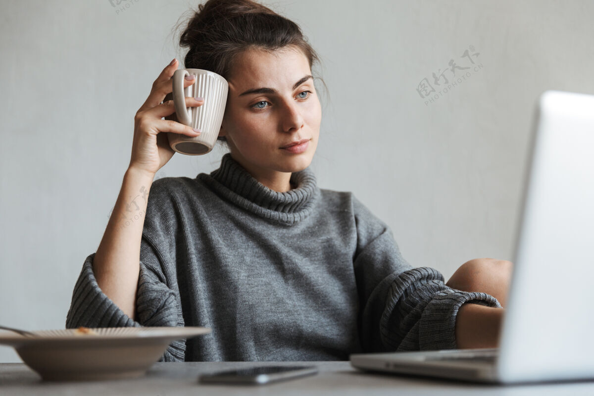 放松坐在厨房里用笔记本电脑吃健康早餐的年轻漂亮女人聊天积极黑发