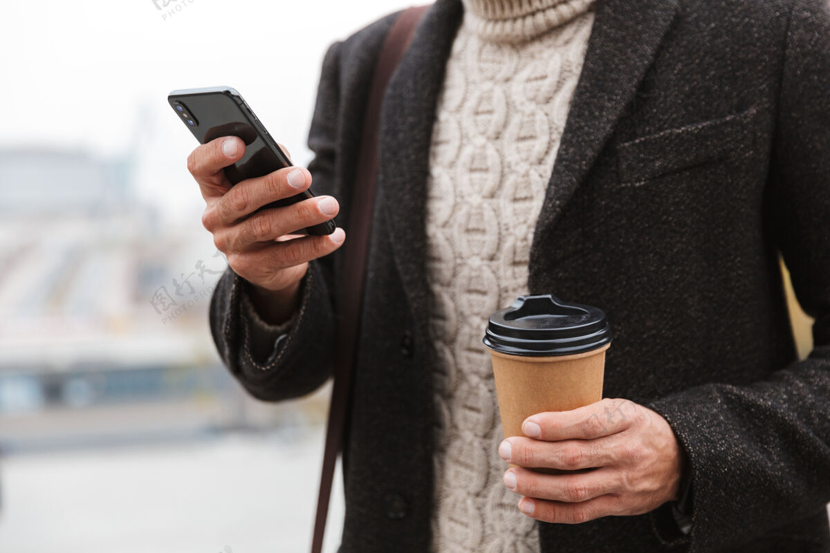 手机30多岁的成年男子穿着夹克 手持手机 端着外卖咖啡 走在城市街道上中心成人休闲