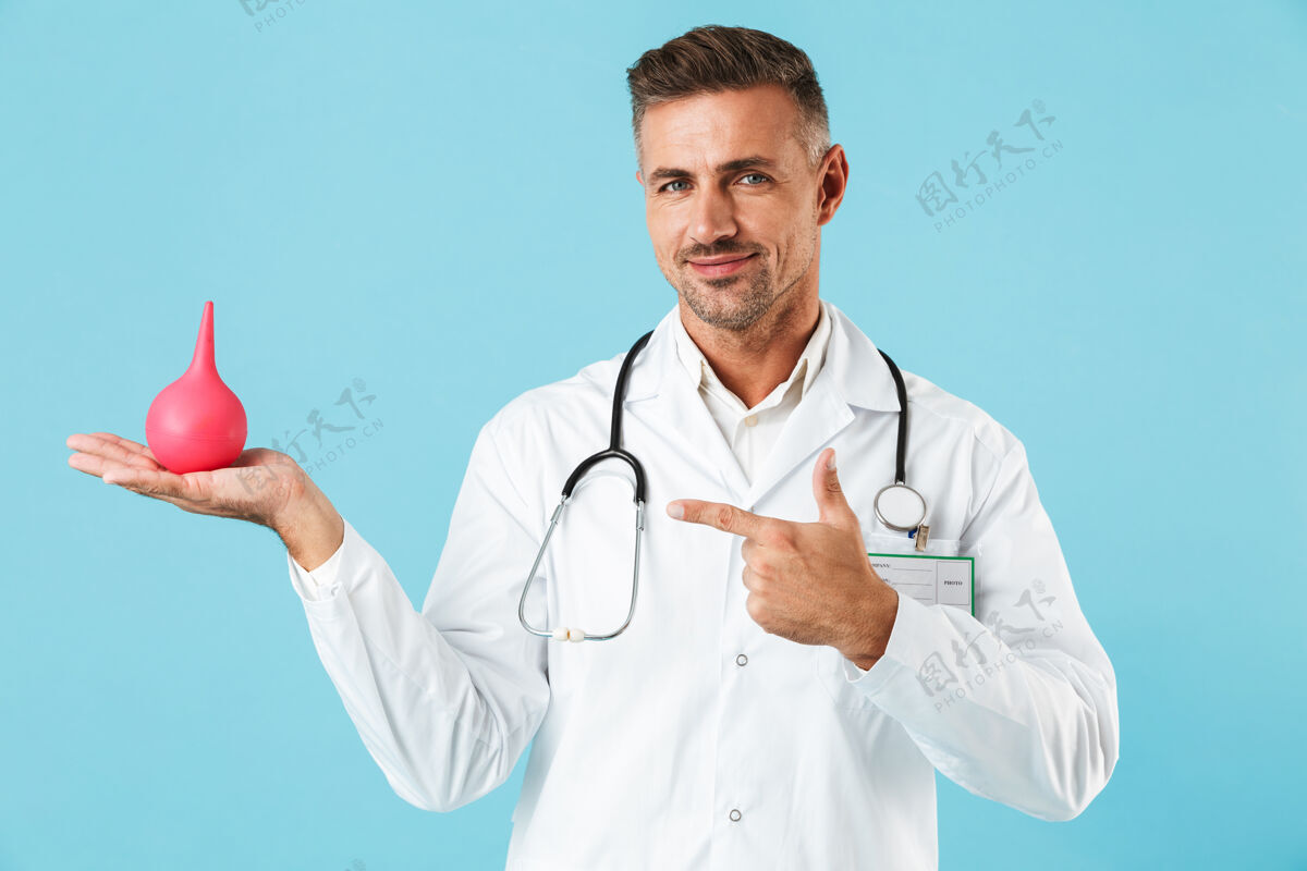 听诊器中年医学专家的画像 身穿白大褂 手持灌肠器 孤立地站在蓝色的墙上医疗救护车治疗