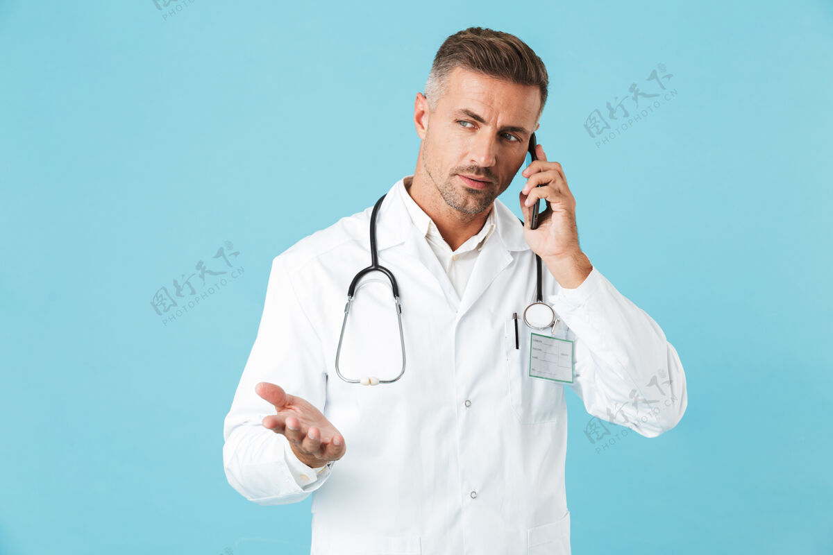 男人照片中 一位身穿白大褂 手持听诊器的成熟医生正在讲手机 孤零零地站在蓝色的墙上救护车手机讲话