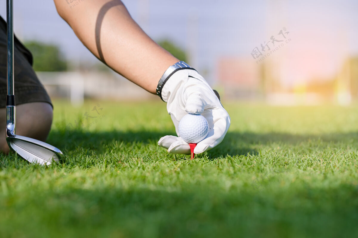 手指手戴手套把高尔夫球放在球场的球座上游戏背景球道