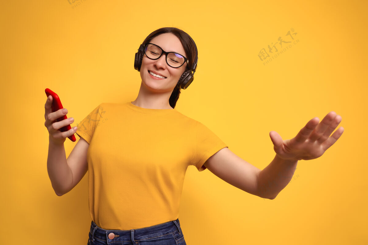 女人摄影棚拍摄了一位身穿黄色t恤 戴着无线耳机的黑发美女 她在黄色的舞台上聆听着响亮的音乐 翩翩起舞女孩无线舞蹈