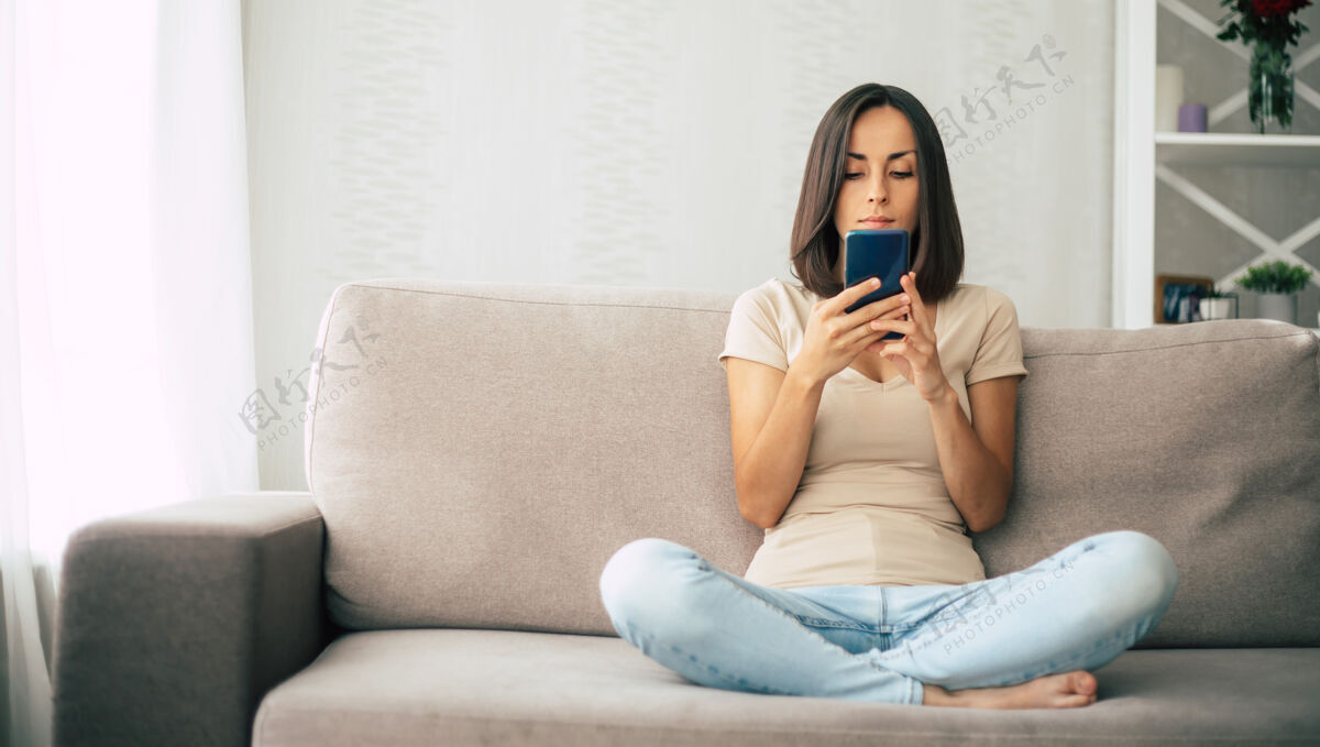 技术年轻的现代自信微笑的女人在家工作或放松 坐在沙发上用智能手机生活欢乐放松