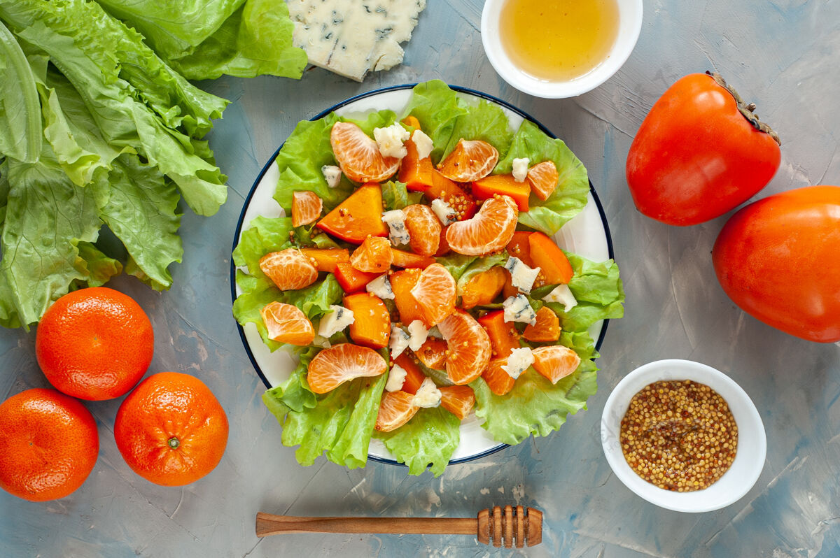 清淡甜酸沙拉配柿子 橘子和蓝奶酪冬季维生素沙拉和配料放在蓝色的桌子上减肥食品从上面看俯视图午餐新鲜