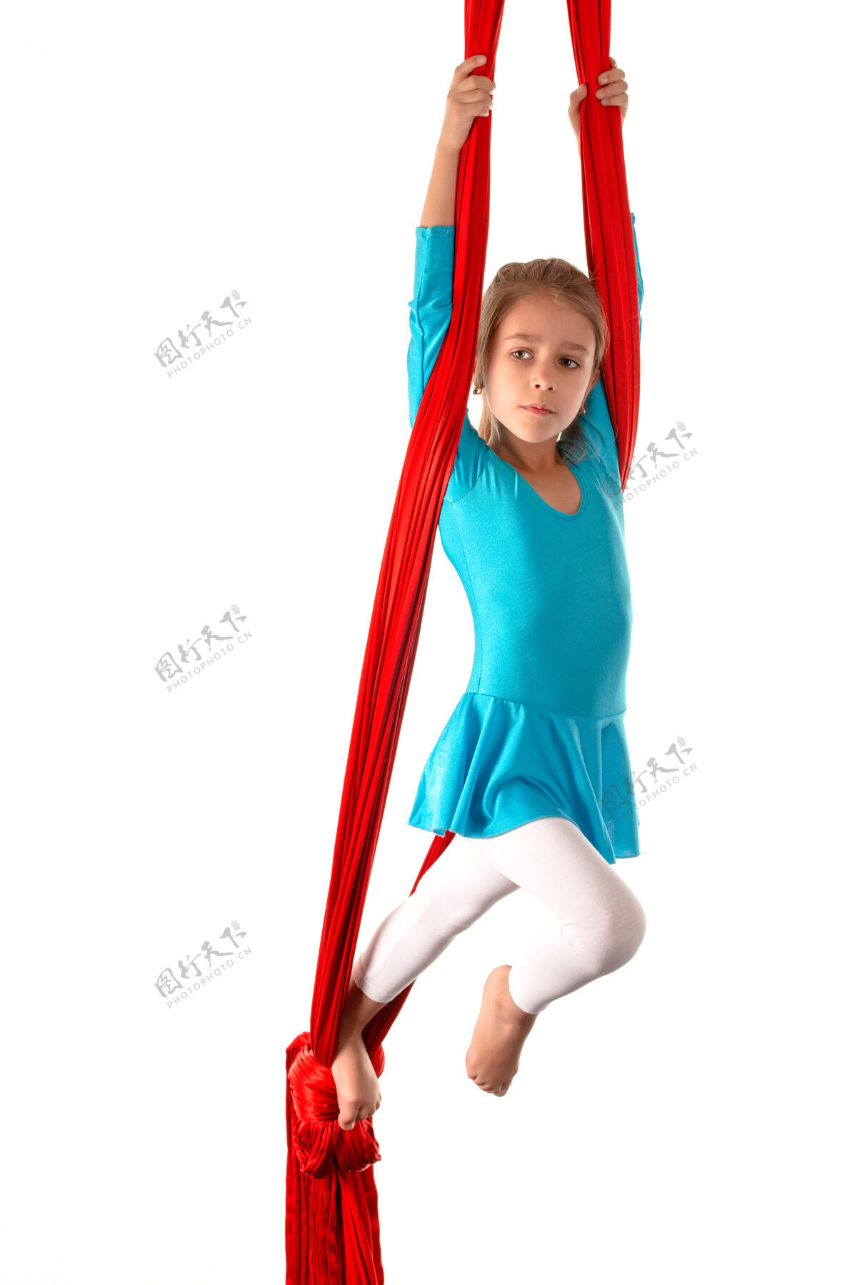 设备一个穿着蓝色泳衣的高加索小女孩 在白色沙滩上的红色飘带上做体操吊床平衡体操