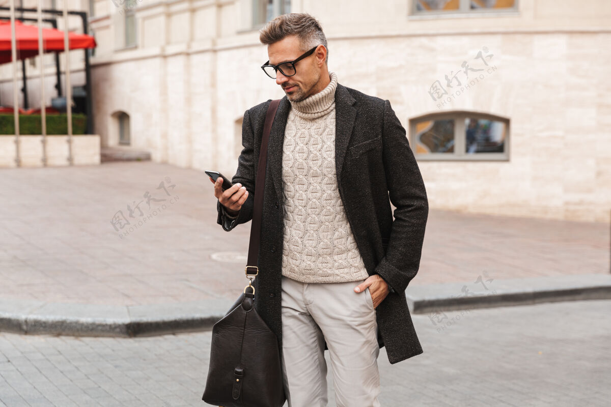 信息帅哥穿着外套走在户外 手里拿着手机休闲街道外套