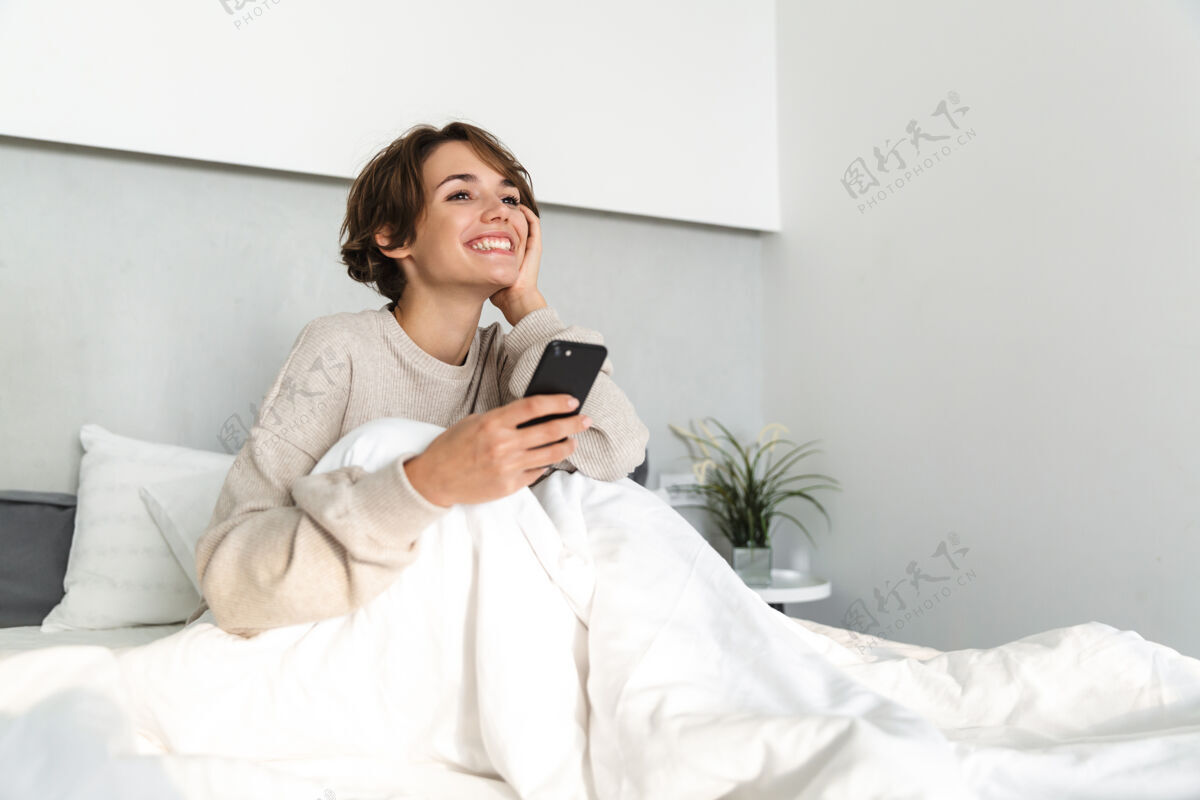 在线微笑的年轻女孩 早上在床上放松 用手机吸引力放松谎言