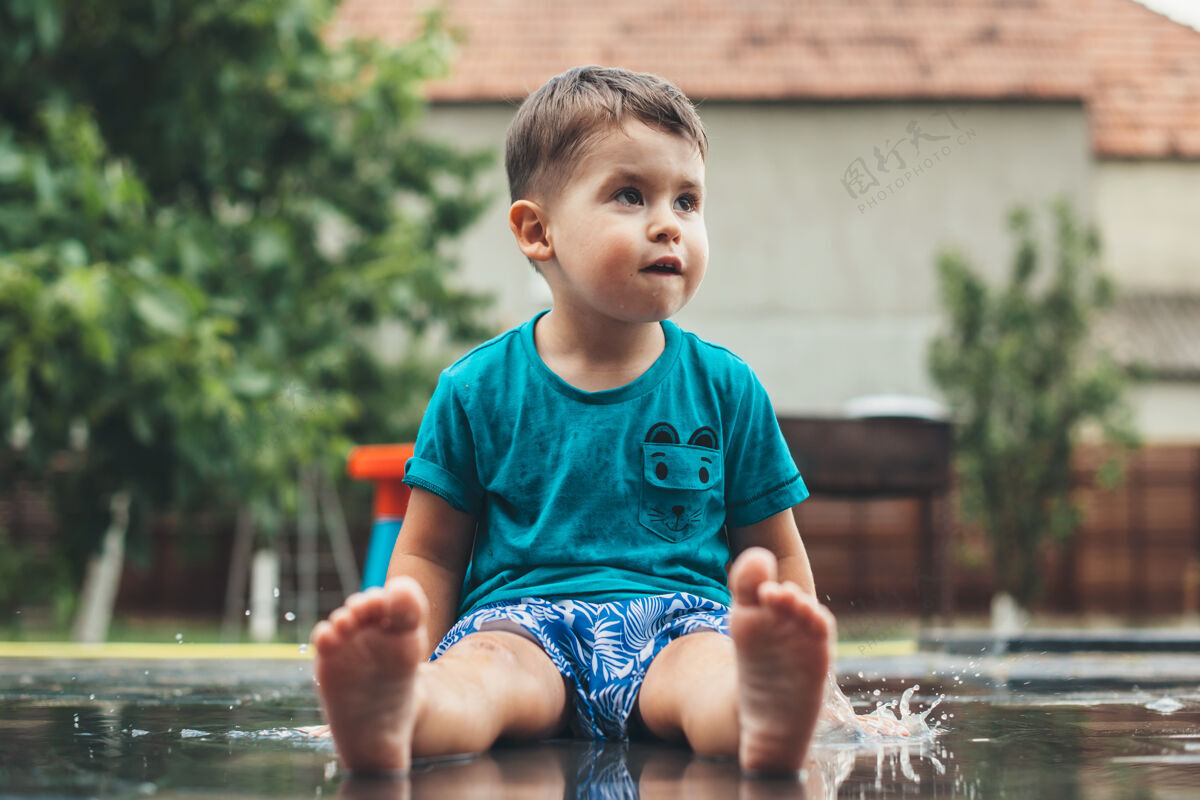 孩子可爱的白人男孩躺在地上的水看起来高兴的东西穿蓝色衣服院子看家庭
