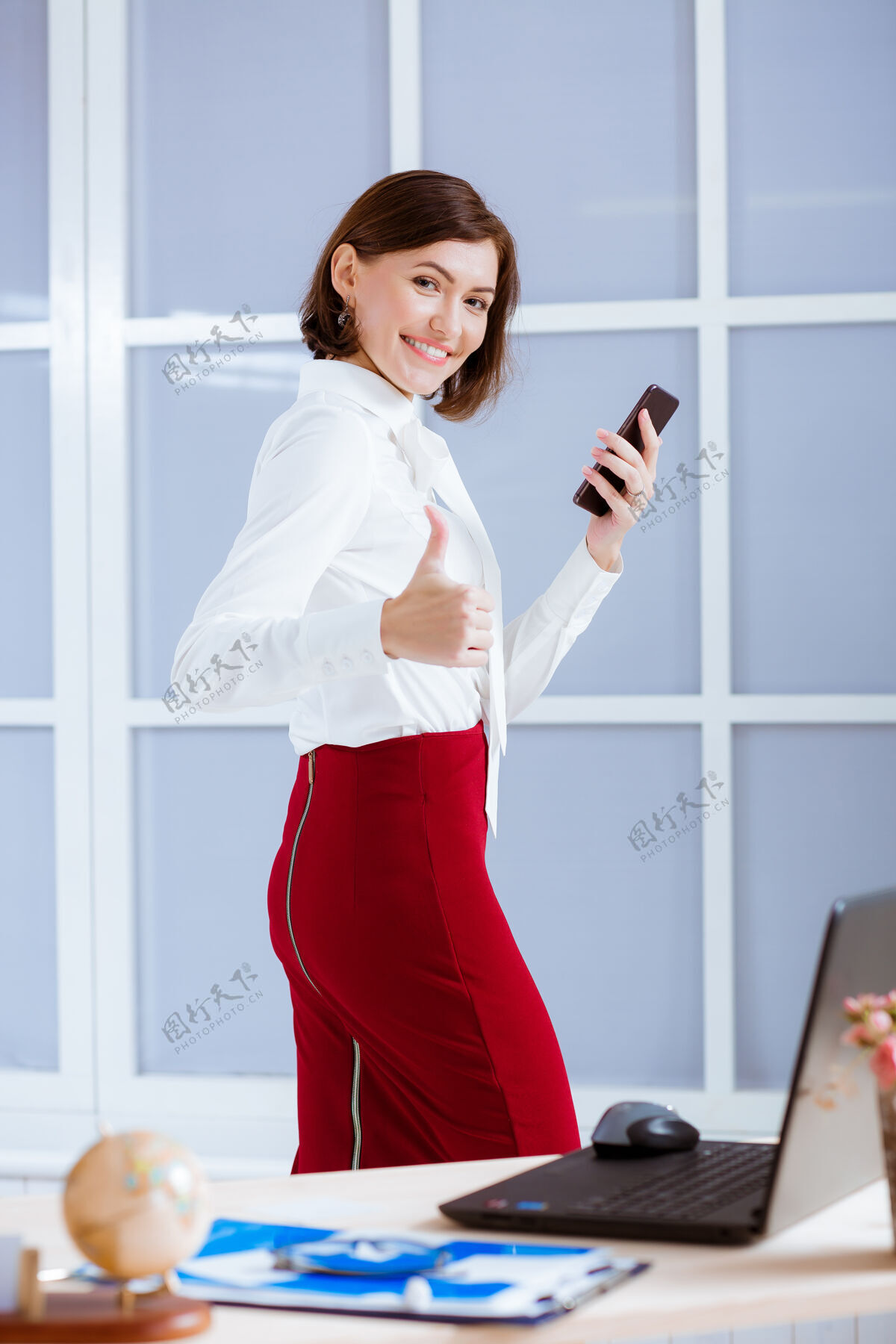 办公室优雅的女商人在办公室竖起大拇指工作场所手机快乐