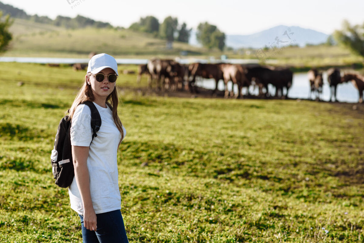 自然背着背包的女旅行者站在农场的马背上乡村女性帽子