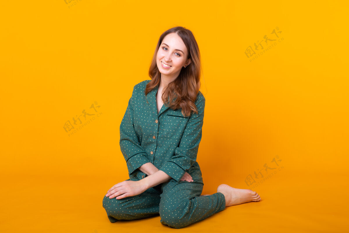年轻穿着睡衣的年轻女子微笑着摆姿势 独自在黄色的墙上休息睡眠女孩睡衣